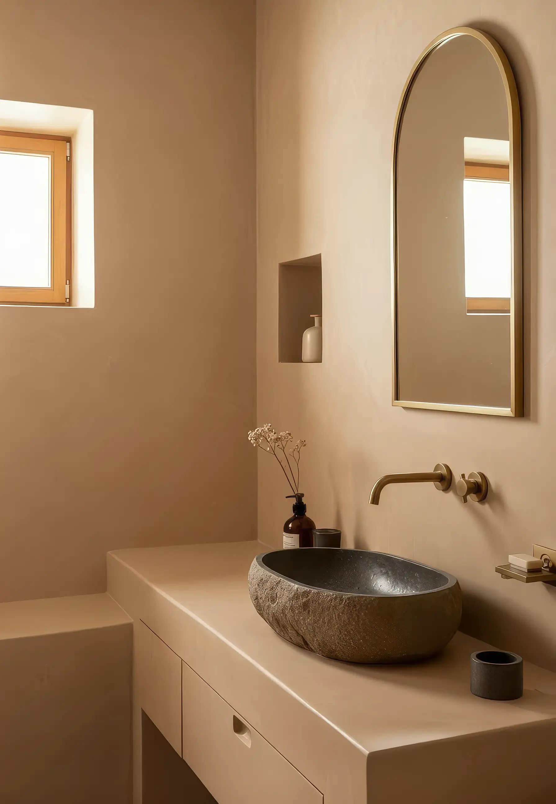 Stone basin on a plaster vanity beneath an arched brass mirror