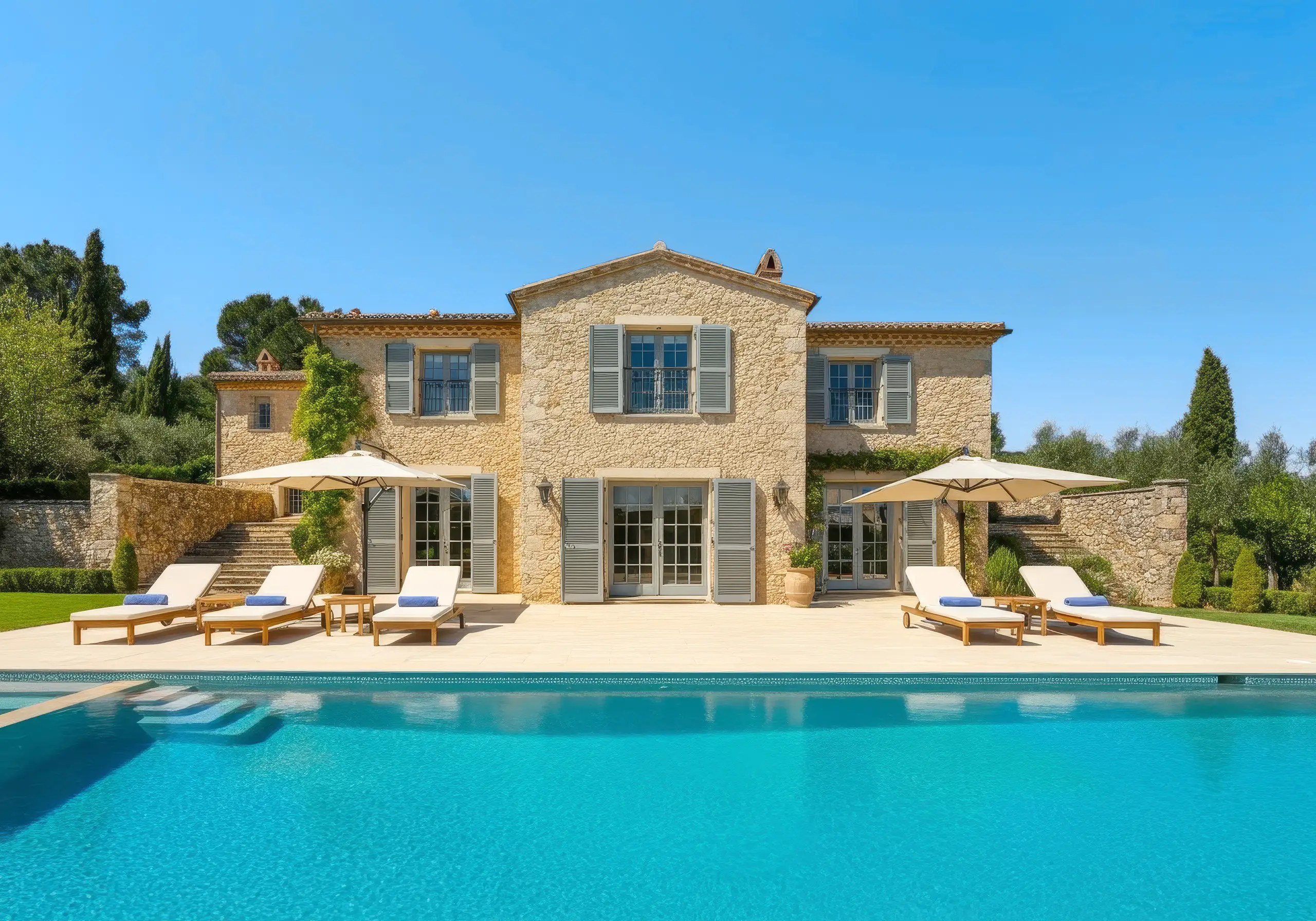 Stone villa with grey shutters, sun loungers and parasols beside a turquoise pool