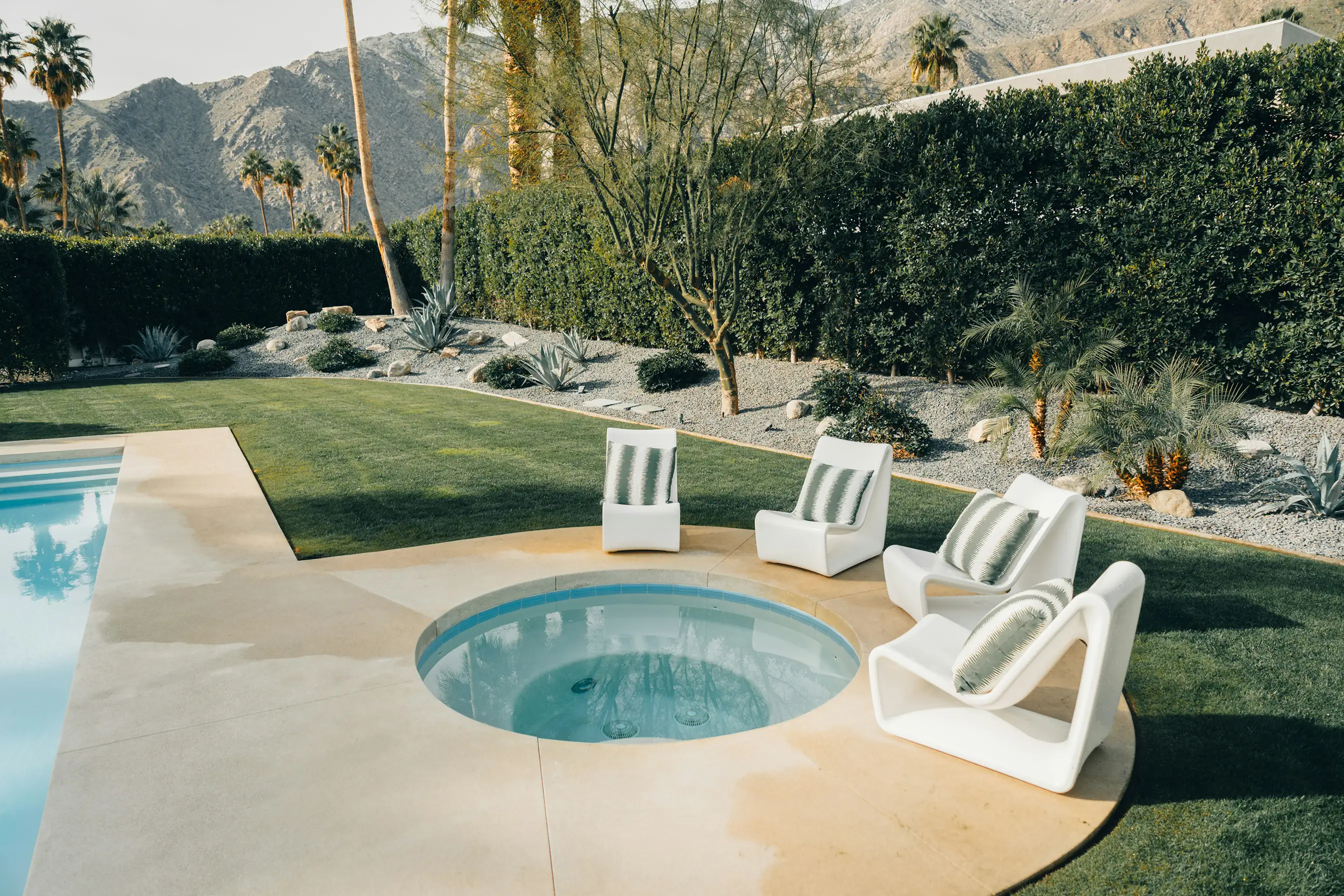 Round spa and white lounge chairs on a lawn by the pool, with palm trees and mountains
