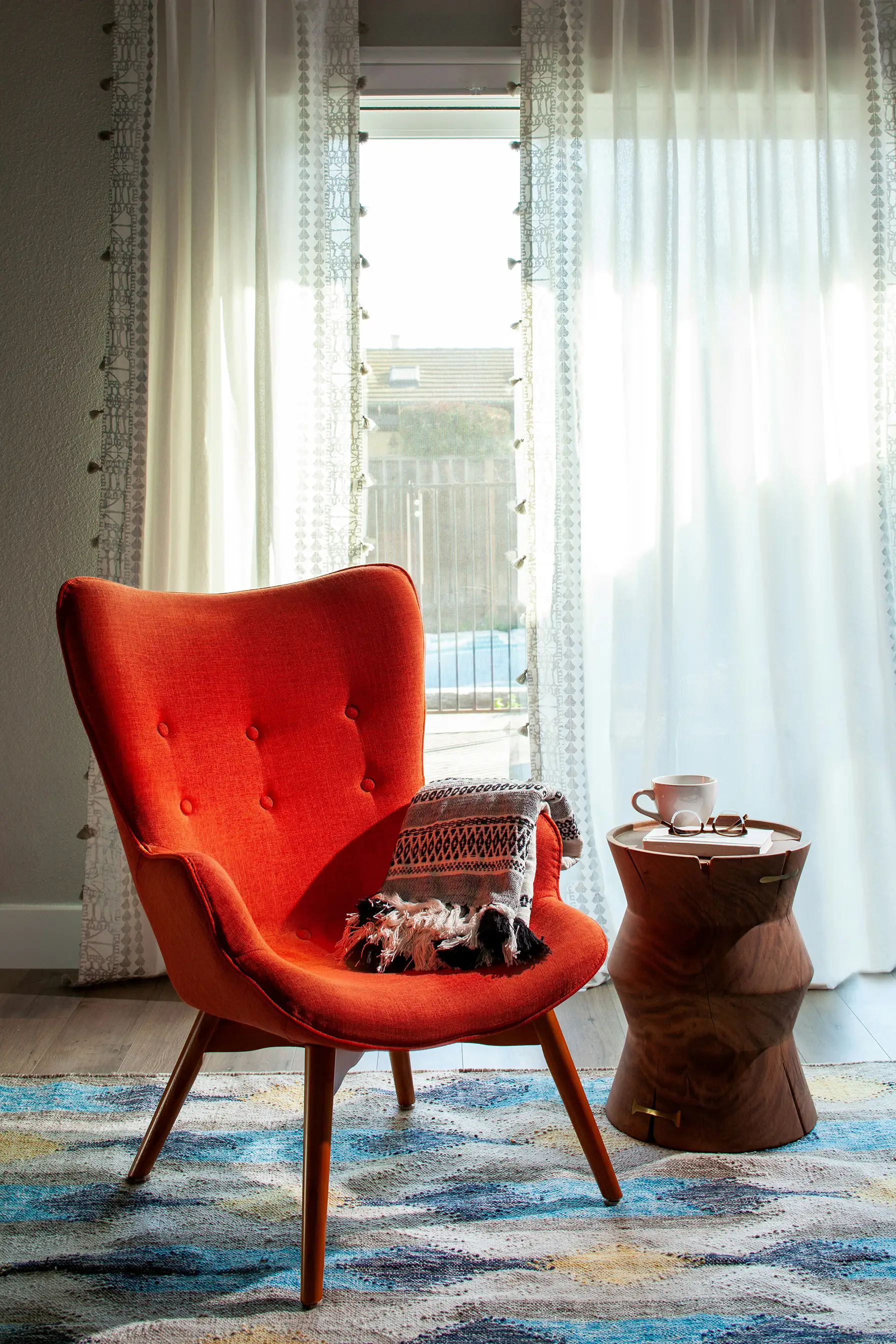 Orange wingback armchair beside a sheer-curtained window