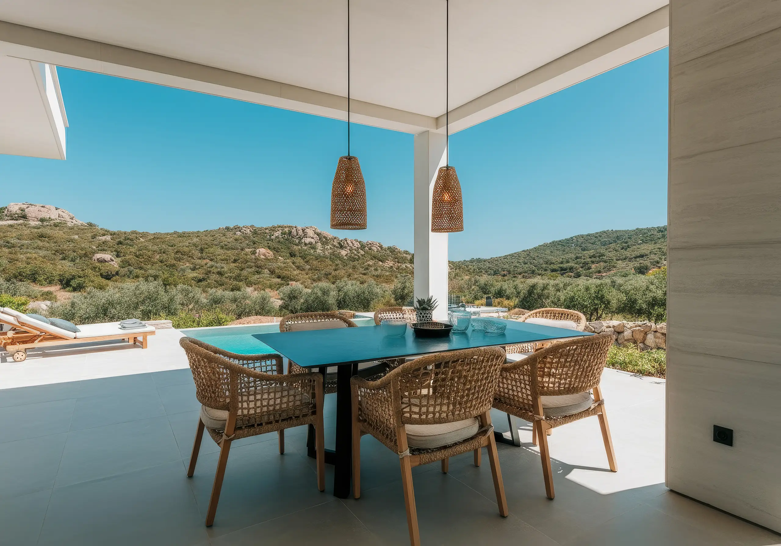 Covered terrace with a dining table and rattan chairs overlooking green hills